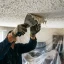 Handyman scraping textured popcorn ceiling material off a ceiling